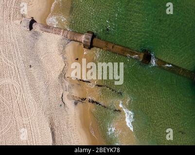 Arrugginito pipeline sulla spiaggia di Ipanema esposto da una forte onda di marea che ha lavato via molta sabbia della spiaggia. Vista dall'alto dell'oggetto industriale Foto Stock