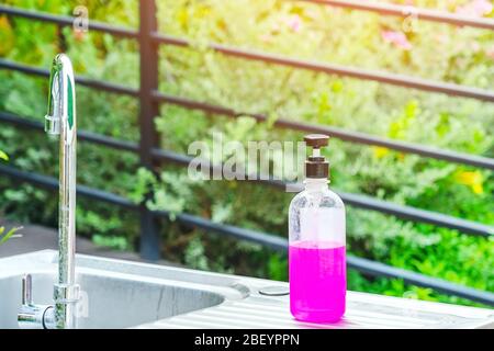Flacone di gel di alcool rosa o detergente antibatterico sui lavelli di alluminio in giardino, gel di alcool per la pulizia della mano per prevenire la diffusione di germi e. Foto Stock