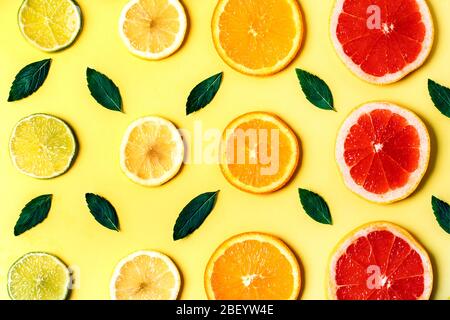 Fette di agrumi, limone e pompelmo e erbe di menta su sfondo giallo. Vista dall'alto. Sfondo di design minimale. Foto Stock