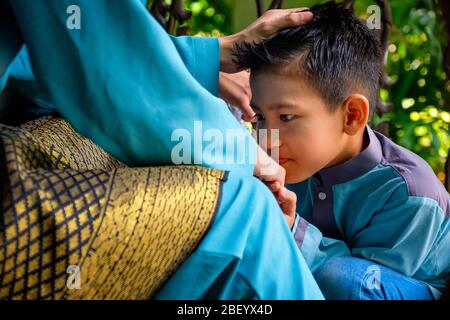 Primo piano di malay figlio musulmano in costume tradizionale mostrando scusa gesto al suo genitore durante la celebrazione Aidilfitri. Raya e atti di moda musulmana Foto Stock