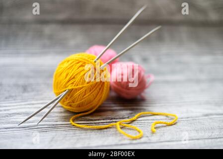 Piatto di tre palle di lana colorate, aghi di maglia che posano sullo sfondo di legno. Foto Stock