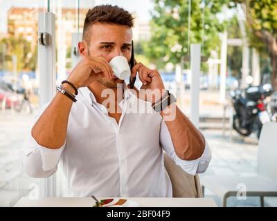 Giovane uomo bere caffè mentre parla sul telefono cellulare Foto Stock