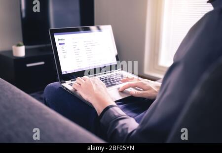Uomo che legge le e-mail e usa il laptop nel salotto di casa. Controllo della posta elettronica Web ricevuta e risposta ai messaggi. Casella di posta in arrivo mockup. Foto Stock