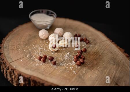 Cioccolato bianco caramellato fatto in casa, cocco e nocciole su una fetta di log. Tartufi caramella palla di neve Foto Stock