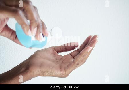 Messa a fuoco selettiva sulla mano sinistra di una donna nera. Mano destra sfocata che trattiene un gel igienizzante. Disinfezione. Foto Stock