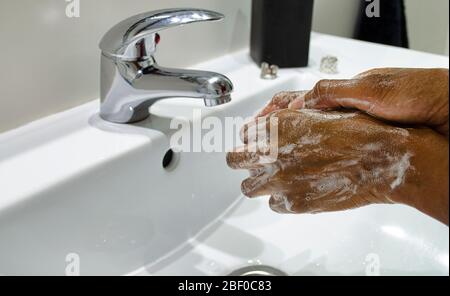 Donna nera che lava coscienziosamente le mani con sapone. Messa a fuoco selettiva sulle mani. Disinfezione. Concetto di igiene. Foto Stock