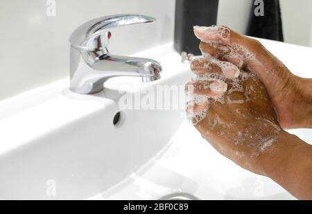Donna nera che lava coscienziosamente le mani con sapone. Messa a fuoco selettiva sulle mani. Disinfezione. Concetto di igiene. Foto Stock