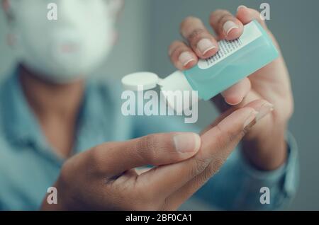 Messa a fuoco selettiva sulle mani di una donna nera che tiene un gel igienizzante e indossa una maschera FFP3. Disinfezione. Coronavirus. Sfondo sfocato. Foto Stock