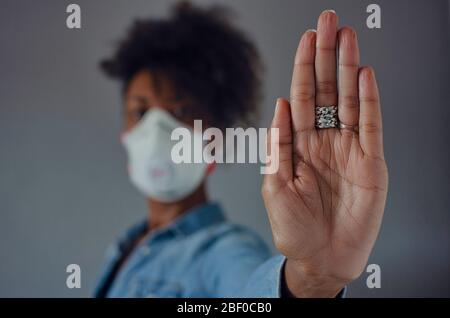 Donna nera che indossa una maschera FFP3 e mostra il palmo della mano come un gesto di stop. Fermare la diffusione di coronavirus. Foto Stock