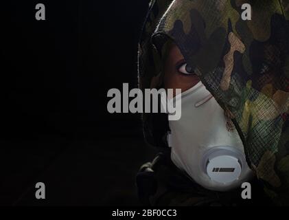 Foto concettuale di una donna guerriera che indossa una maschera FFP3 e un involucro di testa camuffato. Guerra biologica. Arma letale del coronavirus. Messa a fuoco selettiva su Foto Stock