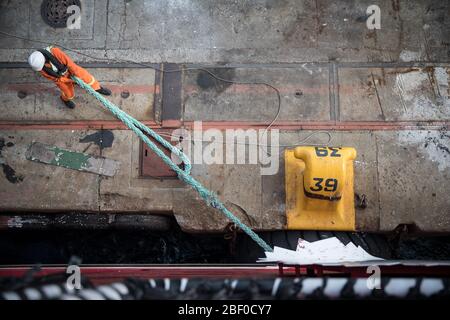 Un lavoratore di ormeggio libera una nave da una scolletta nel porto di Città del Capo, Capo Occidentale, Sud Africa, una trafficata via commerciale, mentre si prepara a salpare. Foto Stock