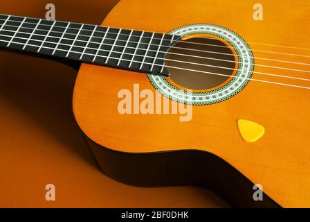 Dettaglio primo piano di una chitarra classica e plettro giallo su sfondo arancione Foto Stock