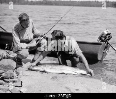 1930 DUE UOMINI PESCATORI E GUIDA MISURA GRANDE PESCE LAGO DEI BOSCHI ONTARIO CANADA - A5145 HAR001 HARS ONTARIO NORTH AMERICA CATTURA TEMPO LIBERO ATTIVITÀ DIVERTIMENTO AVVENTURA HOBBY VIAGGIO INTERESSE E FUGA HOBBY CONOSCENZA PASSIME REEL PIACERE VACANZE GUIDA ANGLING COOPERAZIONE LAGO DEI BOSCHI MID-ADULTO UOMO MEDIO-ADULTO VACANZE RELAX AMATEUR BIANCO E NERO ETNIA CAUCASICA GODIMENTO HAR001 VECCHIO STILE Foto Stock