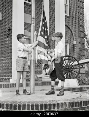 1940S DUE RAGAZZI PRETEEN CHE COOPERANO INNALZANDO BANDIERA AMERICANA SUL FLAGPOLE DI FRONTE AL GOVERNO MATTONE EDIFICIO CANNONE IN BACKGROUND - B12246 HAR001 HARS CELEBRAZIONE FRATELLI CANNONE STATI UNITI COPIA SPAZIO AMICIZIA A TUTTA LUNGHEZZA ISPIRAZIONE STATI UNITI D'AMERICA CARING MASCHI CHE ALZANO FRATELLI FRATELLI B&W GOVERNO LIBERTÀ ALLEGRA FORZA LEADERSHIP ORGOGLIO IN SULLA POLITICA PRETEA FRATELLO SORRISI FLAGPOLE CONCETTUALE GIOIOSO PATRIOTTICO ELEGANTE COOPERATING GIOVANI PRE-TEEN PRE-TEEN RAGAZZO ROSSO BIANCO E BLU STELLE E STRISCE INSIEME NERO E BIANCO ETNIA CAUCASICA HAR001 DAVANTI VECCHIO STILE Foto Stock