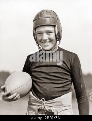 1940S SORRIDENTE PRE-TEEN RAGAZZO ATLETA TENENDO CALCIO INDOSSANDO SQUADRA UNIFORME E CASCO IN PELLE GUARDANDO LA FOTOCAMERA - B1302 HAR001 HARS ATLETICA COPY SPAZIO MEZZA LUNGHEZZA FISICA FITNESS MASCHI RISCHIO ATLETICA FIDUCIA B&W CONTATTO OCCHI OBIETTIVI ATTIVITÀ FELICITÀ FISICA FORZA ED ECCITAZIONE RICREAZIONE ORGOGLIO ATLETI FLESSIBILITÀ MUSCOLI FOOTBALLS CRESCITA GIOVANI PRE-TEEN PRE-TEEN RAGAZZO AMERICANO CALCIO NERO E BIANCO ETNIA CAUCASICA HAR001 VECCHIO STILE Foto Stock