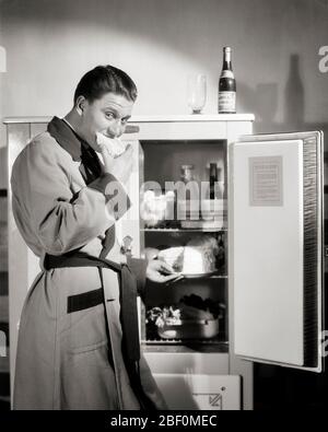 1930 IMBARAZZATO UOMO GUARDANDO MACCHINA FOTOGRAFICA VESTIRE ACCAPPATOIO CATTURATO MANGIARE MEZZANOTTE SNACK FETTA DI TORTA DA FRIGORIFERO BIRRA IN CIMA - F1525 HAR001 HARS B&W CONTATTO OCCHI FETTA FAME FELICITÀ SCOPERTA E NUTRIZIONE CATTURATO SNEAKING DI IMBARAZZATO CONCETTUALE VESTIRE ABITO A TARDA NOTTE CONSUMARE NUTRIMENTO CONSUMANTE LUI ACCAPPATOIO MEZZANOTTE SNACK NOTTE RITORNO GIOVANE UOMO ADULTO NERO E BIANCO ETNIA CAUCASICA HAR001 VECCHIO STILE IN CIMA Foto Stock