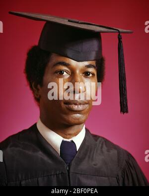 1970 RITRATTO AFRO-AMERICANO UOMO CHE INDOSSA LA CUFFIA DI GRADUAZIONE E GLI ACCAPPATOI GUARDANDO LA MACCHINA FOTOGRAFICA - KS13062 HAR001 HARS AFRO-AMERICANO E CONOSCENZA LEADERSHIP NERO ETNIA ORGOGLIO ISTRUZIONE SUPERIORE COLLEGE MORTARBOARD GIOVANE UOMO CAPPUCCIO E ABITO HAR001 VECCHIO STILE AFRICANO AMERICANI Foto Stock