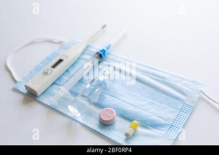 maschera medica su sfondo azzurro. maschera viso. maschera per malattie. Termometro e farmaco. Immagine facciale monouso. Bendaggio respiratorio medico viso. Concetto di quarantena del coronavirus. Foto Stock