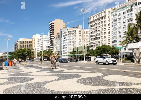 Padre e figlia in bicicletta sul viale Copacabana con il tipico modello di piastrelle portoghesi durante l'epidemia del virus Corona COVID-19 Foto Stock