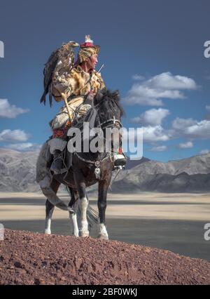 Cacciatore di aquile mongolo, giri kazaki con aquila addestrata a cavallo di fronte alle montagne, provincia di Bajan-Oelgii, Mongolia Foto Stock