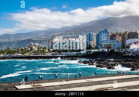 La gente del posto pesca e guarda le onde giganti che si infrangono sulla riva del porto di Puerto de la Cruz mentre la nebbia di calima scende dal monte Teide. Foto Stock