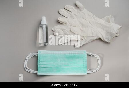 Vista dall'alto del kit di protezione antiepidemia, mazzette, guanti e flacone igienizzante per mani imbevuto di alcool su sfondo grigio Foto Stock