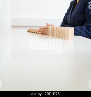 Vista ad angolo basso di businesswoman che ferma il crollo dominos con la sua mano in un'immagine concettuale di gestione depressione di affari. Foto Stock