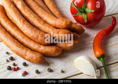 Mazzo di salsicce affumicate sottili vicino ai pomodori, peperoni rossi caldi e aglio su un tavolo di legno. Salsicce tradizionali nella nutrizione quotidiana. Vista dall'alto. Foto Stock