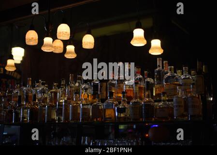Le luci a soffitto illuminano una varietà di alcolici in bottiglie che fiancheggiano la parete in un bar Foto Stock