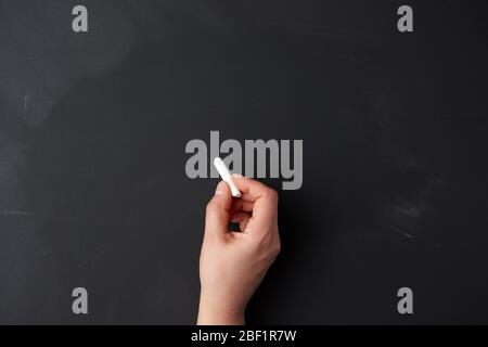 la mano tiene un pezzo di gesso bianco sullo sfondo di un bordo nero vuoto gesso, concetto di presentazione, di ritorno a scuola Foto Stock