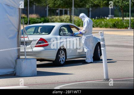 Sugar Land, Texas - 16 aprile 2020: Vestito con completo equipaggiamento protettivo un operatore sanitario raccoglie informazioni da anziani coppia seduta all'interno del loro Foto Stock