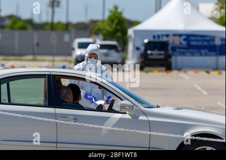 Sugar Land, Texas - 16 aprile 2020: Vestito con completo equipaggiamento protettivo un operatore sanitario raccoglie informazioni da anziani coppia seduta all'interno del loro Foto Stock