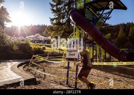 NORTH VANCOUVER, BC, CANADA - Apr 11, 2020: I bambini giocano fuori di un parco giochi chiuso in un parco pubblico di North Vancouver fiancheggiato da nastro di attenzione Foto Stock