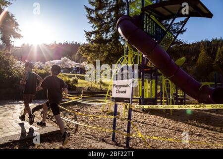 NORTH VANCOUVER, BC, CANADA - Apr 11, 2020: I bambini giocano fuori di un parco giochi chiuso in un parco pubblico di North Vancouver fiancheggiato da nastro di attenzione Foto Stock