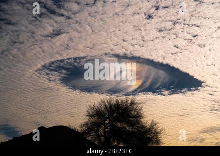 Fallstreak buchi con arcobaleni in altocumuli nuvole che assomiglia a navicelle nel cielo mattutino Foto Stock