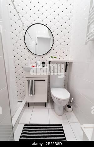 Parte di un piccolo bagno nuovo e moderno. I colori principali - bianco e nero. Pareti e pavimenti piastrellati. Armadietto con lavandino, ripiano, specchio, wc Foto Stock