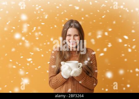 Bella giovane donna con caffè caldo e caduta di neve su sfondo colore Foto Stock