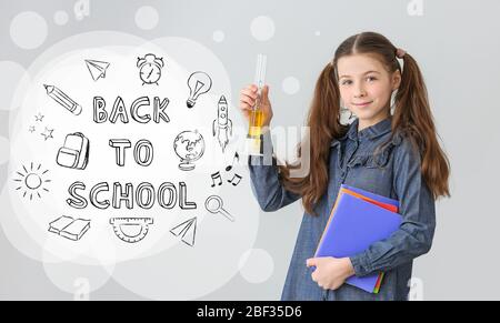 Bambina con vetreria da laboratorio e testo A SCUOLA SU sfondo grigio Foto Stock