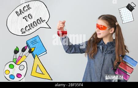 Piccola scolaretta con vetreria da laboratorio e testo A SCUOLA SU sfondo grigio Foto Stock