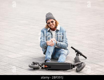Giovane uomo caduto fuori dal suo scooter da calcio all'aperto Foto Stock