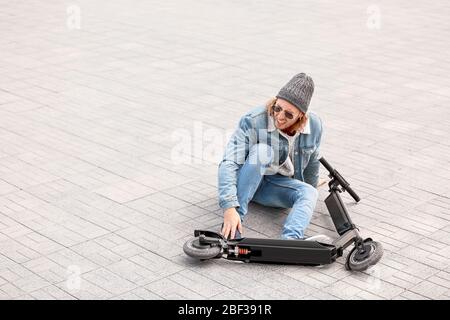 Giovane uomo caduto fuori dal suo scooter da calcio all'aperto Foto Stock