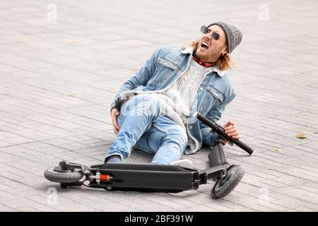 Giovane uomo caduto fuori dal suo scooter da calcio all'aperto Foto Stock