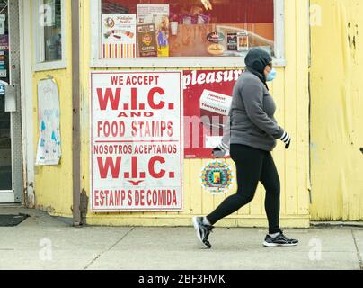 16 aprile 2020, Chelsea, Massachusetts, USA: Donna a piedi da WIC cibo timbro segni al minimarket a Chelses durante la pandemia COVID-19. Chelsea ha la concentrazione più alta di casi COVID-19 in Massachusetts. Più del 60% dei residenti di Chelsea sono Latino e quasi la metà sono immigrati. Foto Stock