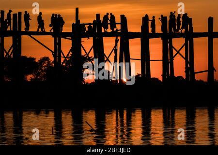 Monaci e turisti si riuniscono sul ponte U Bein al tramonto a Mandalay, Myanmar Foto Stock