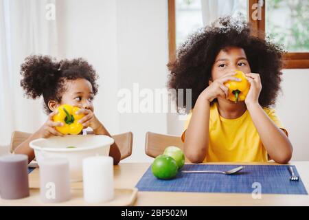 Piccola sorella più giovane carina che guarda domandarsi e imitato la sua sorella più vecchia provare a mangiare peperone Foto Stock