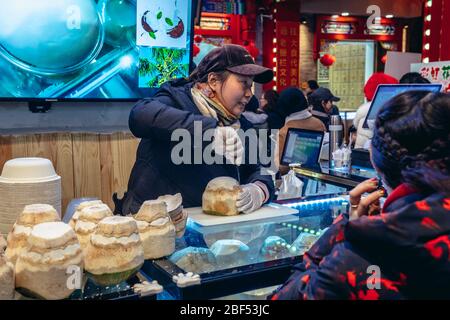 Donna che spacca il cocco a Dashilan Commercial Street nella zona di Qianmen Street nel distretto di Dashilan di Pechino, Cina Foto Stock