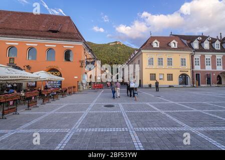 Edifici su Piata Sfatului - Piazza del Consiglio a Brasov, il centro amministrativo della contea di Brasov, Romania, vista con Tampa montagna sullo sfondo Foto Stock