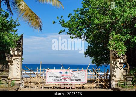 Kuta, Bali Island, Indonesia - 16 aprile 2020: Bandiera con segnale di avvertimento sul cancello d'ingresso alla spiaggia chiuso per impedire la diffusione di focolai di coronavirus. Foto Stock