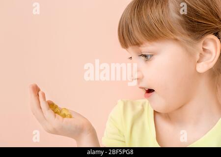 Bambina con pillole di olio di pesce su sfondo colore Foto Stock