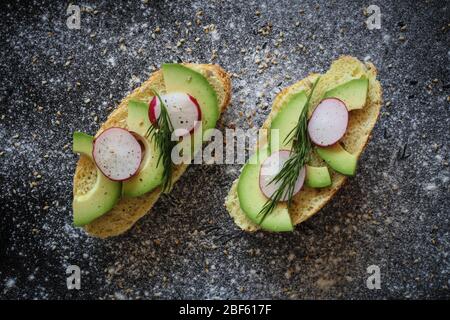 Panini vegani fatti di rotolo di pane di mais con avocado, ravanello e aneto su sfondo nero cosparso di farina Foto Stock
